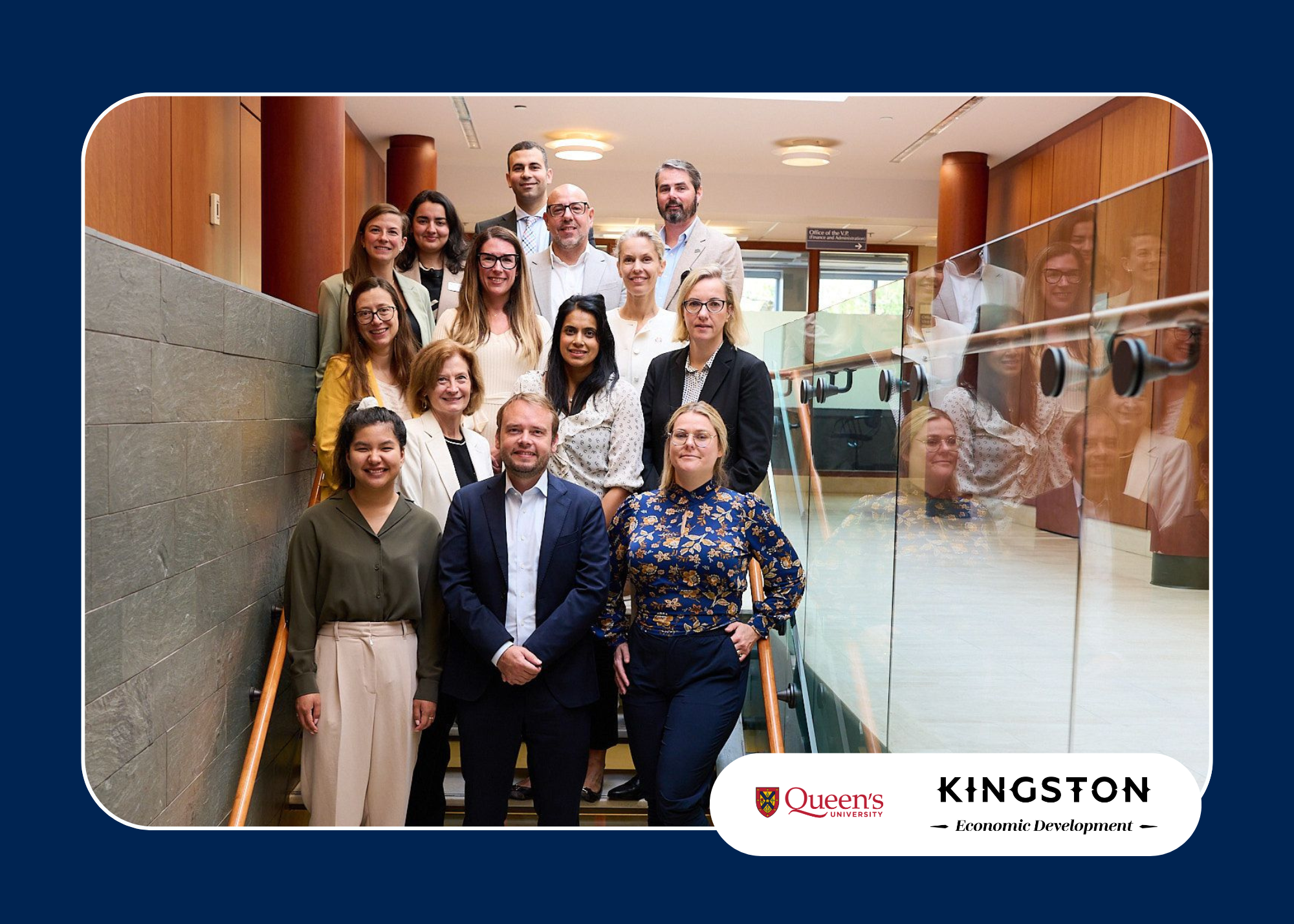 Group of professionals posing on a staircase during a diplomatic visit, with Queen's University and Kingston Economic Development logos displayed.