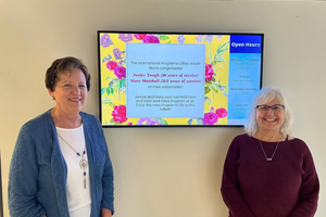 Photo of Mary and Janice standing in front of a TV announcing their retirement from the International Programs Office