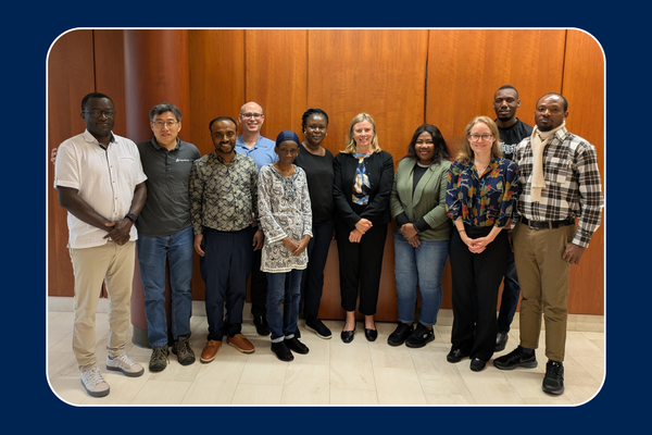 Group of 11 individuals stand in front of wall in Richardson Hall, Queen's blue background framing photo