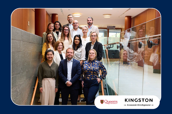 Group of professionals posing on a staircase during a diplomatic visit, with Queen's University and Kingston Economic Development logos displayed.