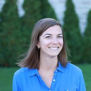 Csilla Smiling, Woman in Blue Shirt in Front of Green Background