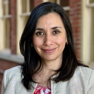 Alejandra Perez Headshot, smiling with brick wall behind her