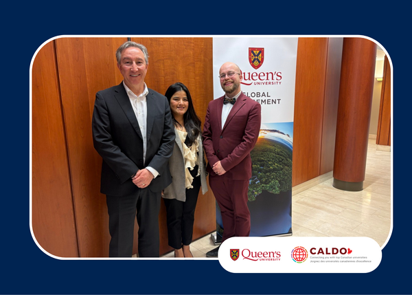 Three people stand indoors beside a Queen's University Global Engagement banner, posing for a photo. Queen's University and CALDO logos appear at the bottom right.