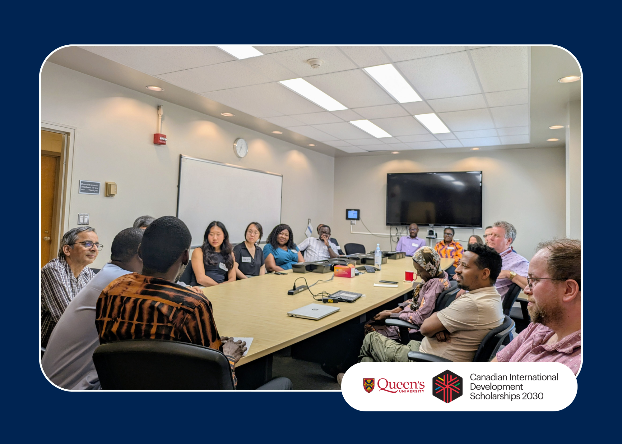 Group of people seated around a conference table in a meeting room with Queen's University and CID Scholarships 2030 logos.