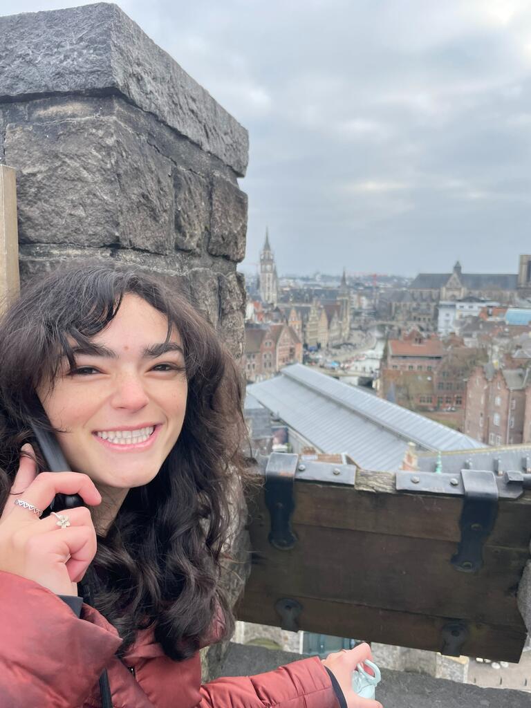 Student is standing in a castle smiling before the view of the city.