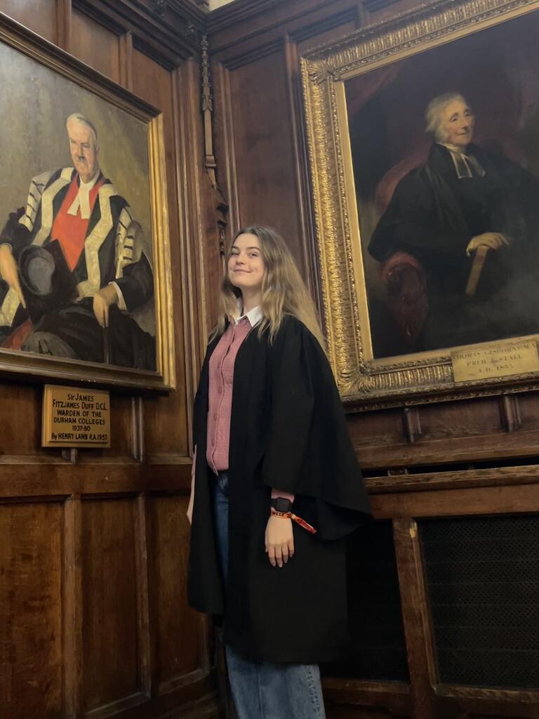 Patricia is standing with some historic portraits at school