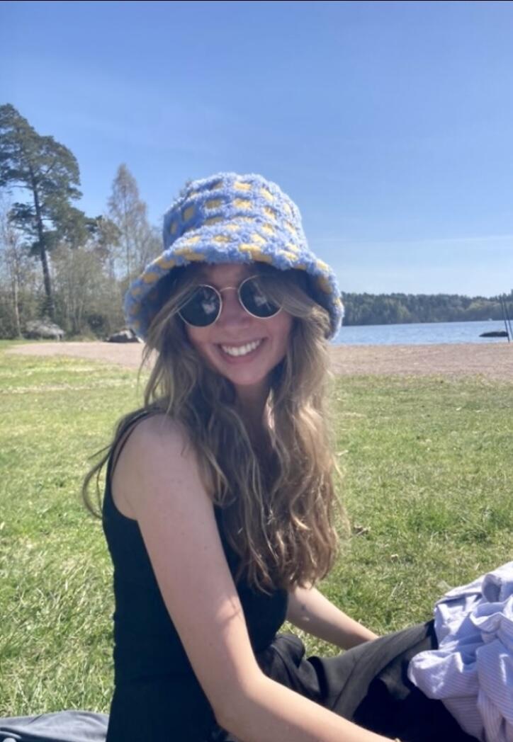Alice smiling for the camera wearing a fuzzy bucket hat and sitting on a patch of grass