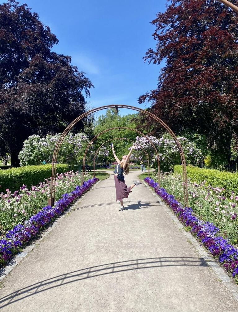 Alice posing with her arms to the sky in front of flowers