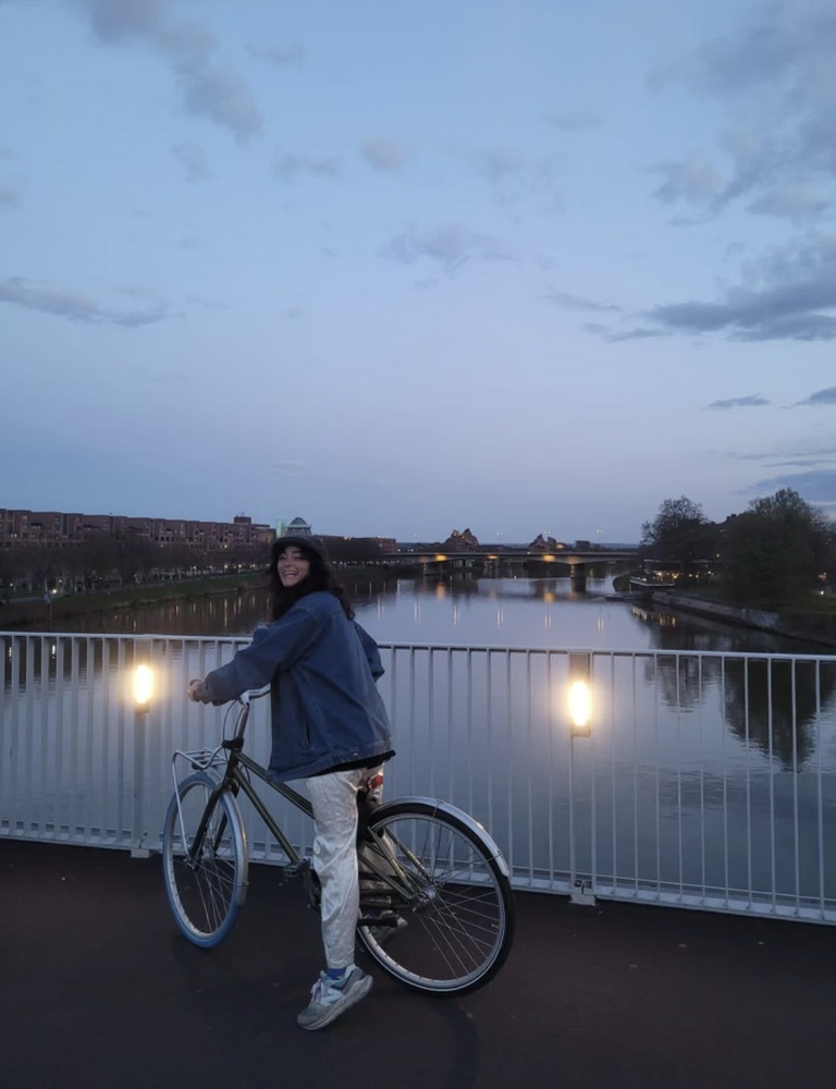 Student is on a bike on a bridge of the river at dusk.