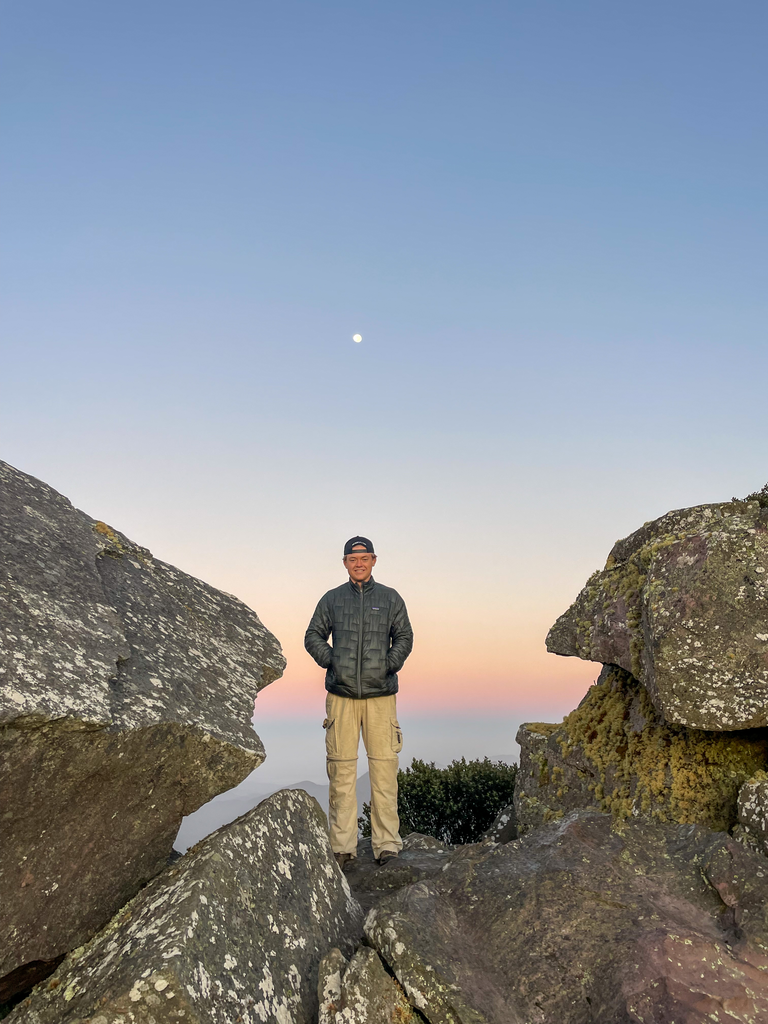 Jack standing on large rocks with a colourful sky and the moon visibly behind