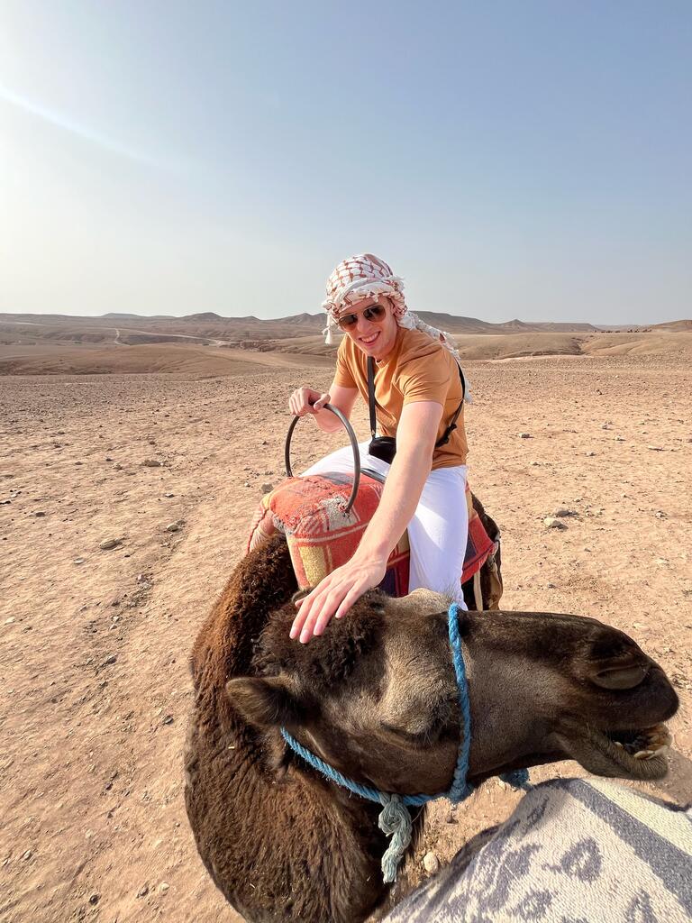 Andrew sits on a camel smiling towards the camera