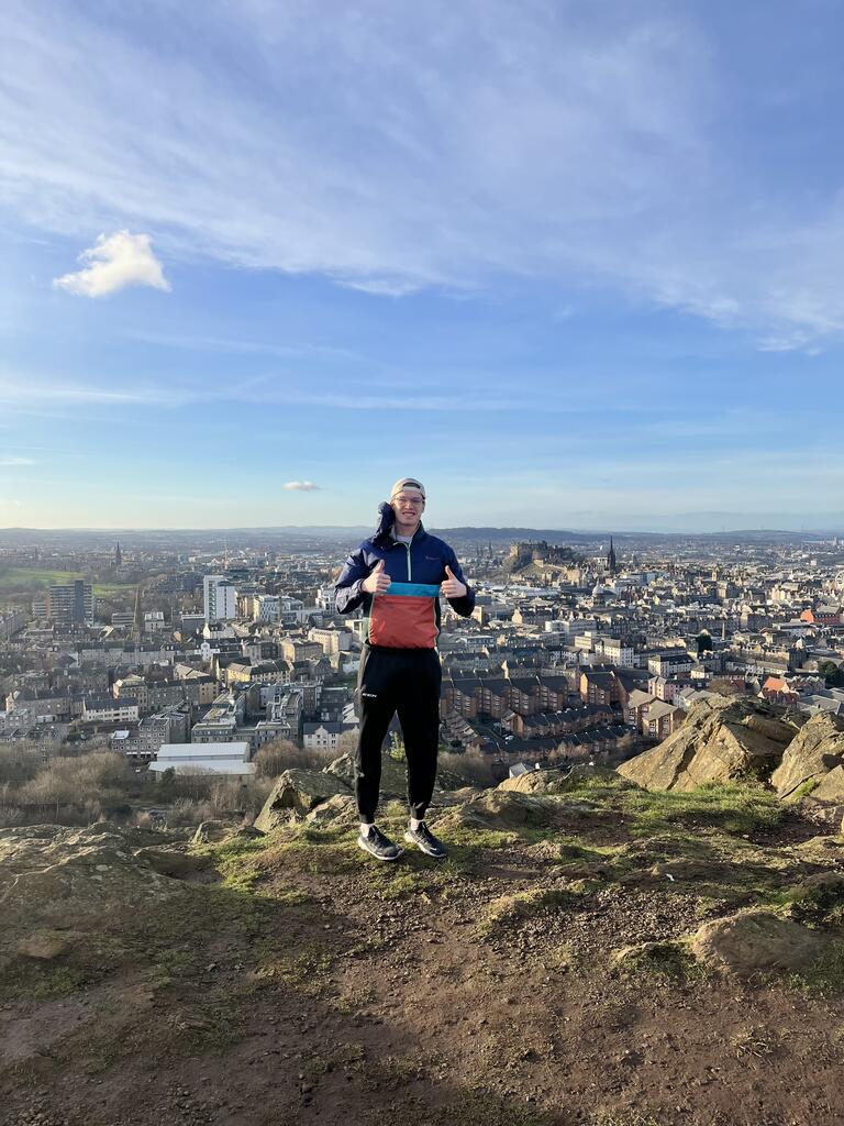 Andrew standing with thumbs up in front of a view of Edinburgh