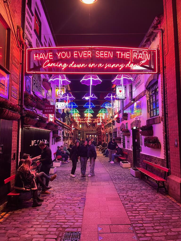 Emily and friends standing in front of a neon sign in a busy cobble stoned street