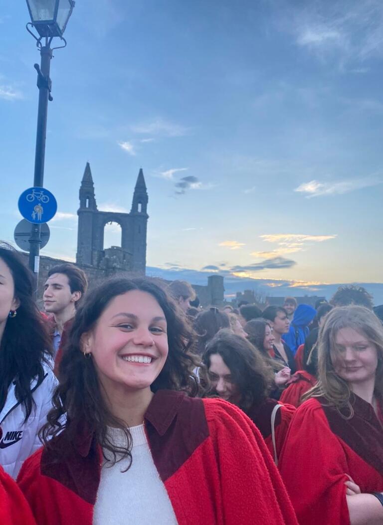 Valerie stands in a red robe with friends on a sunny day