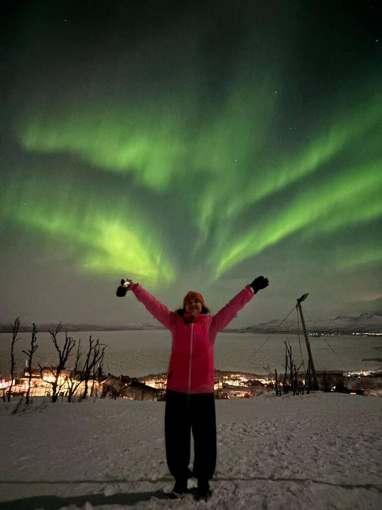 Solomiia is standing beneath the Northern Lights with her hands to the sky and snow on the ground.