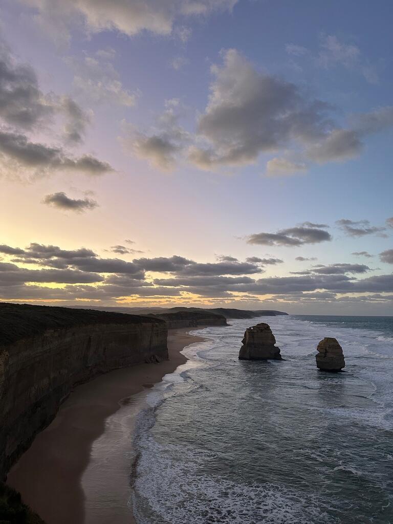 Dramatic coastal scene at dusk with towering sea stacks, rolling waves, and rugged cliffs under a sky transitioning from soft pink to deep blue. Tranquil and majestic.