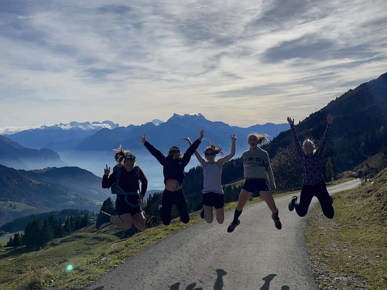 Alyssa and friends jumping in the air with arms outstretched, with mountains and water in the background.