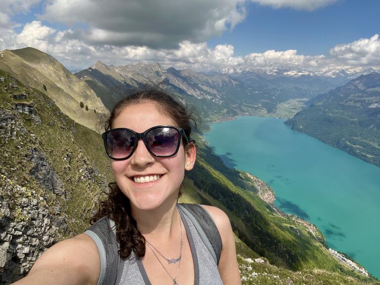 Alyssa hiking on a sunny day with mountains and water in the background.
