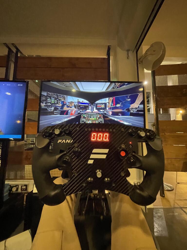 Jazib playing a racing simulator using a black steering wheel and pedals. The screen shows a detailed race car cockpit view, creating an immersive experience.
