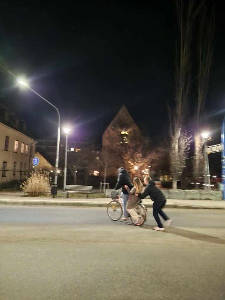 A candid capture of two people riding a bicycle, and another pushing from behind