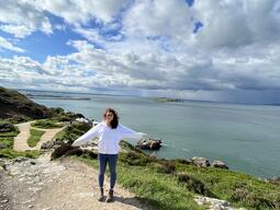Michelle is standing by a cliff by a body of water