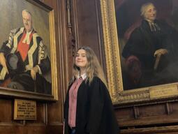 Patricia is standing with some historic portraits at school
