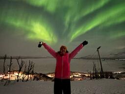 Solomiia is standing beneath the Northern Lights with her hands to the sky and snow on the ground.