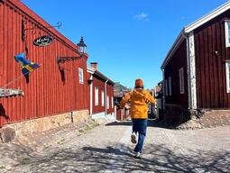 Solomiia is running a yellow jacket, with a blue sky, and red barns