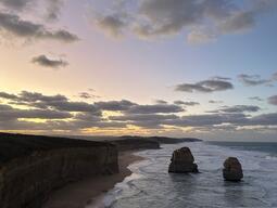 Dramatic coastal scene at dusk with towering sea stacks, rolling waves, and rugged cliffs under a sky transitioning from soft pink to deep blue. Tranquil and majestic.