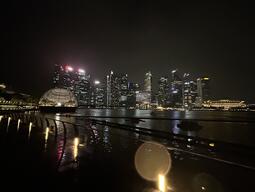 A nighttime cityscape with a luminous skyline reflects in the water. A glowing domed structure stands out. The scene conveys a serene, vibrant atmosphere.