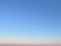 A panoramic view of a city skyline at sunrise, with a clear blue sky and warm light casting a golden glow on tall buildings and a river below, conveying serenity.
