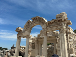 A crowd of tourists gathers in front of an ancient stone archway at archaeological ruins under a clear blue sky, evoking curiosity and awe.