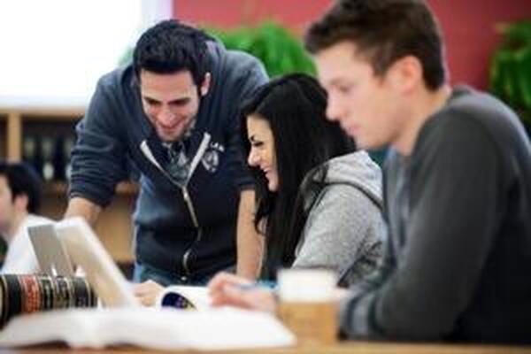 three students studying, with one student helping the other