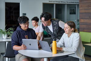 3 students chatting and two have laptops open. 