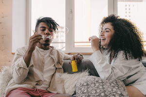 two people sitting on the couch, one is blowing bubbles