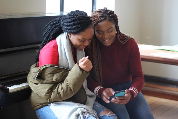 two students talking and reading something on a cell phone. 