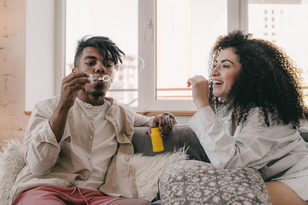 two people sitting on the couch, one is blowing bubbles