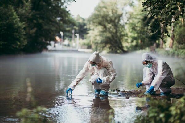 Two people in coveralls collecting water in glass vials