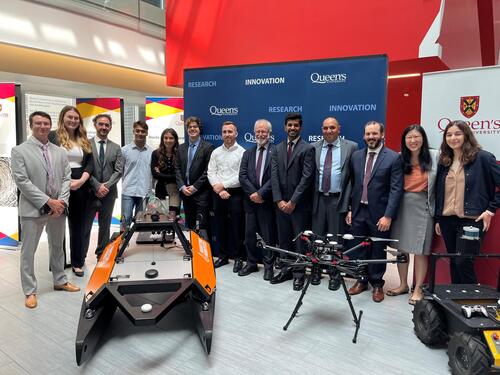 Researchers and Queen's Principal standing around Ingenuity Labs robots