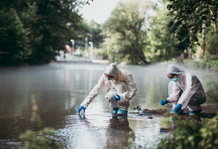 Two people in coveralls collecting water in glass vials