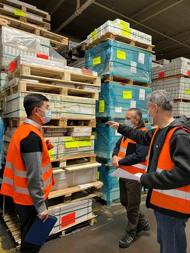 Ohanna founders wearing orange vests are standing in a warehouse holding a meeting