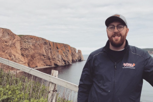 Photograph of Josh Livingstone standing in front of a body of water and cliffs