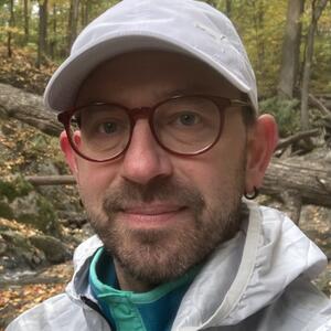 Photograph of Professor Mark Smith in a forest with a backdrop of trees and fallen leaves.