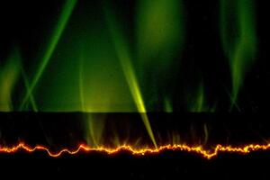 The appearance of green flashing curved lights above a polymer p-n junction. The dark region is the polymer, with the negative side on the bottom and the positive side above. The crooked orange line represents electrical treeing. The curved green flashes represent a new discovery; they are caused by electrons interacting with a gas produced by a deteriorating polymer surface.