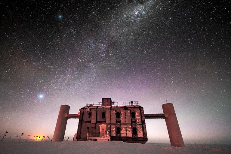 Front view of the IceCube Lab at twilight, with a starry sky showing a glimpse of the Milky Way overhead and sunlight lingering on the horizon. [Credit: Martin Wolf, IceCube/NSF]