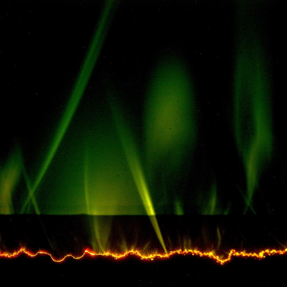 The appearance of green flashing curved lights above a polymer p-n junction. The dark region is the polymer, with the negative side on the bottom and the positive side above. The crooked orange line represents electrical treeing. The curved green flashes represent a new discovery; they are caused by electrons interacting with a gas produced by a deteriorating polymer surface.