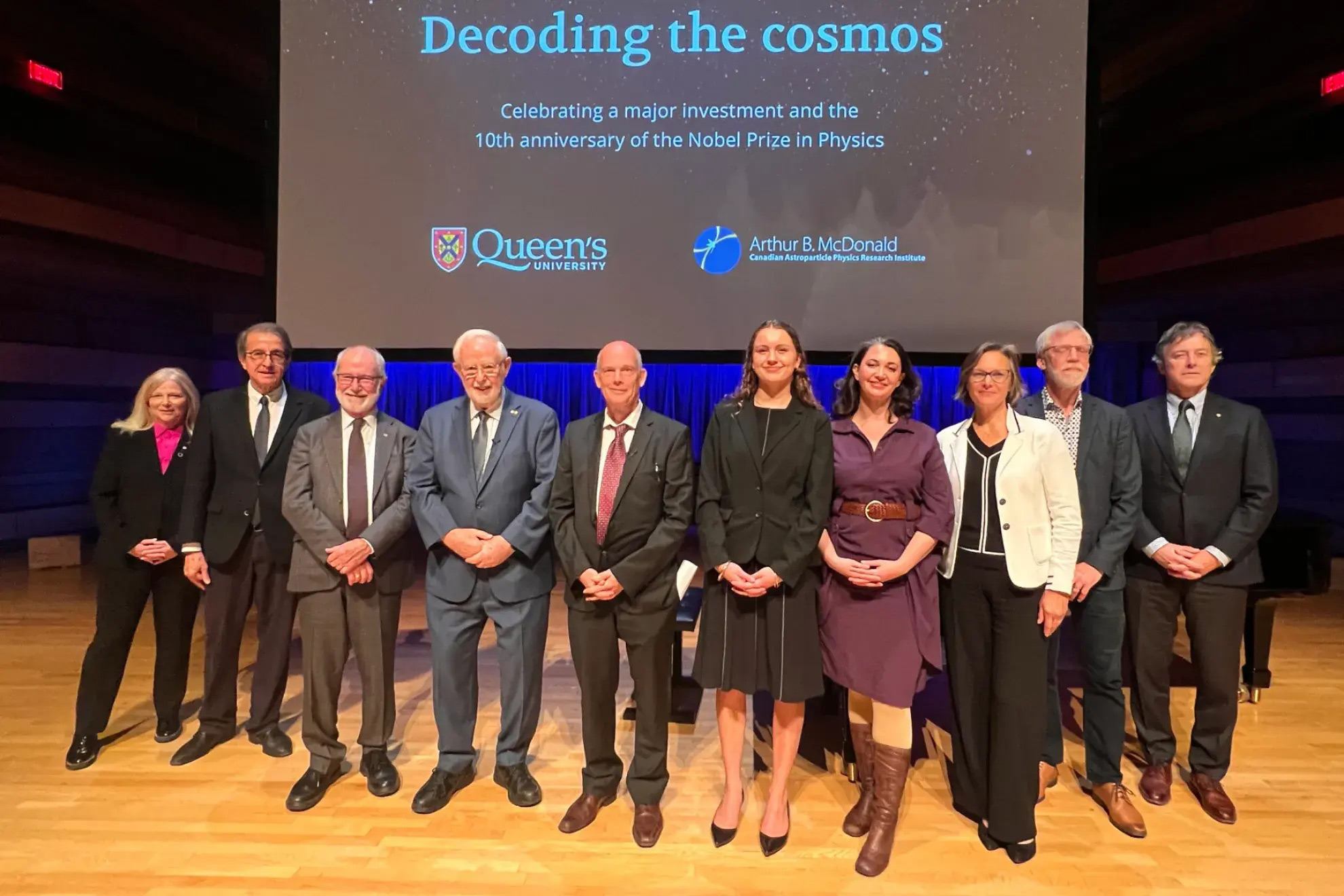 From left to right: Dr. Nancy Ross, Dr. Alejandro Adem, Dr. Patrick Deane, Dr. Art McDonald, Dr. Tony Noble, Julia Brachman, Zoe Brisson-Tsavoussis, Kate Wilson, Dr. John Burge, and Michael Fraser on stage at the Isabel Bader Centre for the Performing Arts. Group