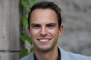 Professor Paul Gardner standing in front of a brick wall, wearing a grey suit, smiling