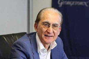 Tariq Modood sitting at a table, wearing a blue suit and white shirt. 