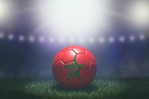 photograph of a red soccer ball with a green star sitting on grass with stadium lights in the background